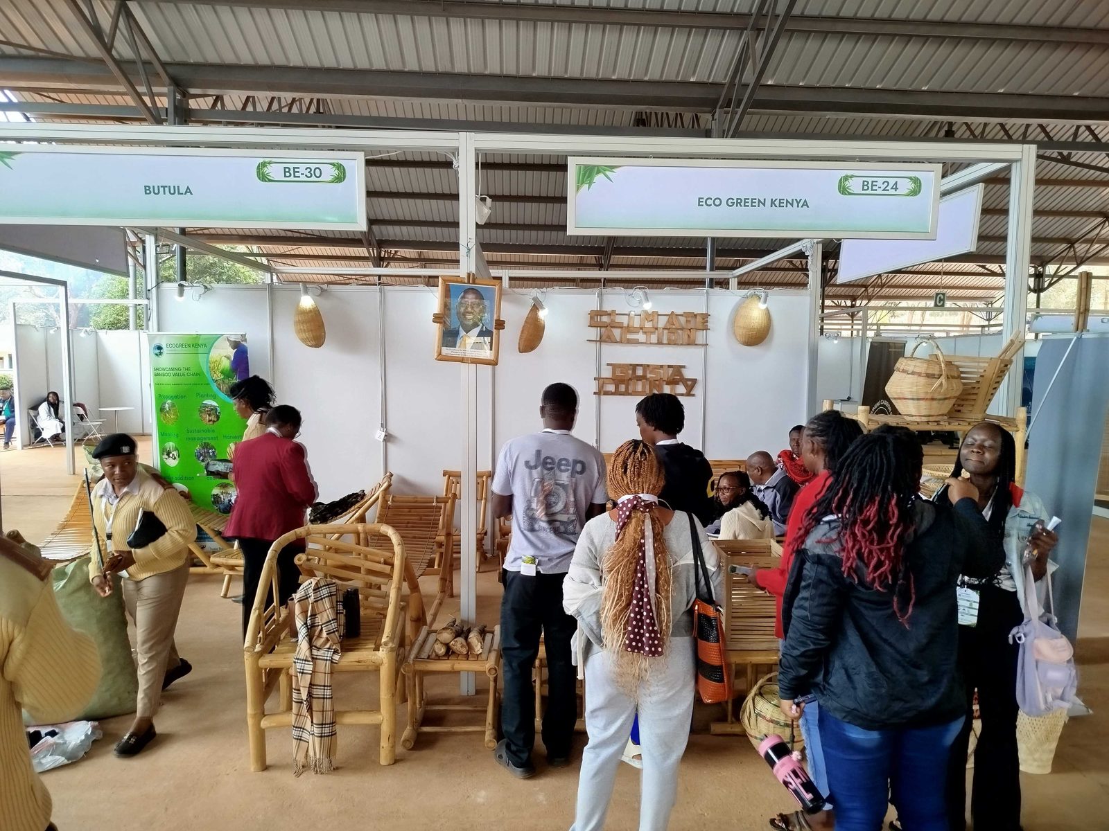 Visitors crowding the EcoGreen Kenya stand at the Bamboo Expo, with bamboo chairs and a Busia County sign made of bamboo.