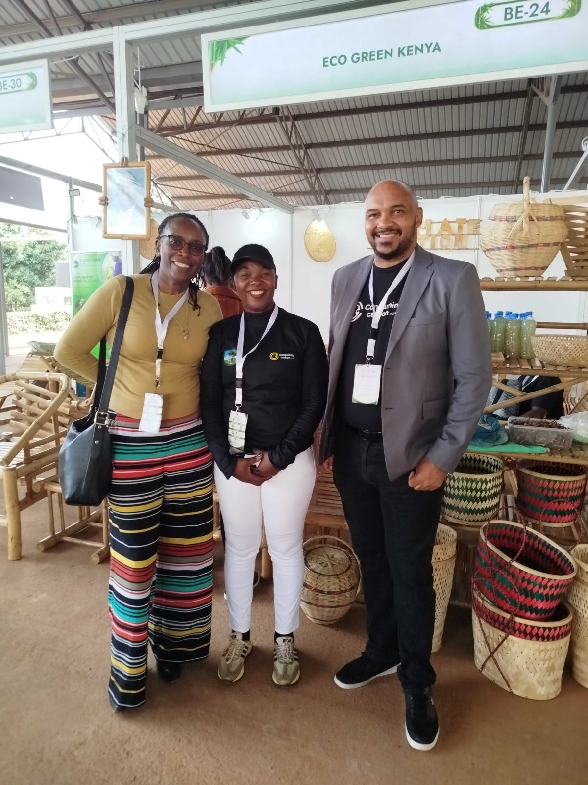 Members of the Consuming Carbon and EcoGreen Kenya team smiling in front of woven bamboo baskets at the stand.