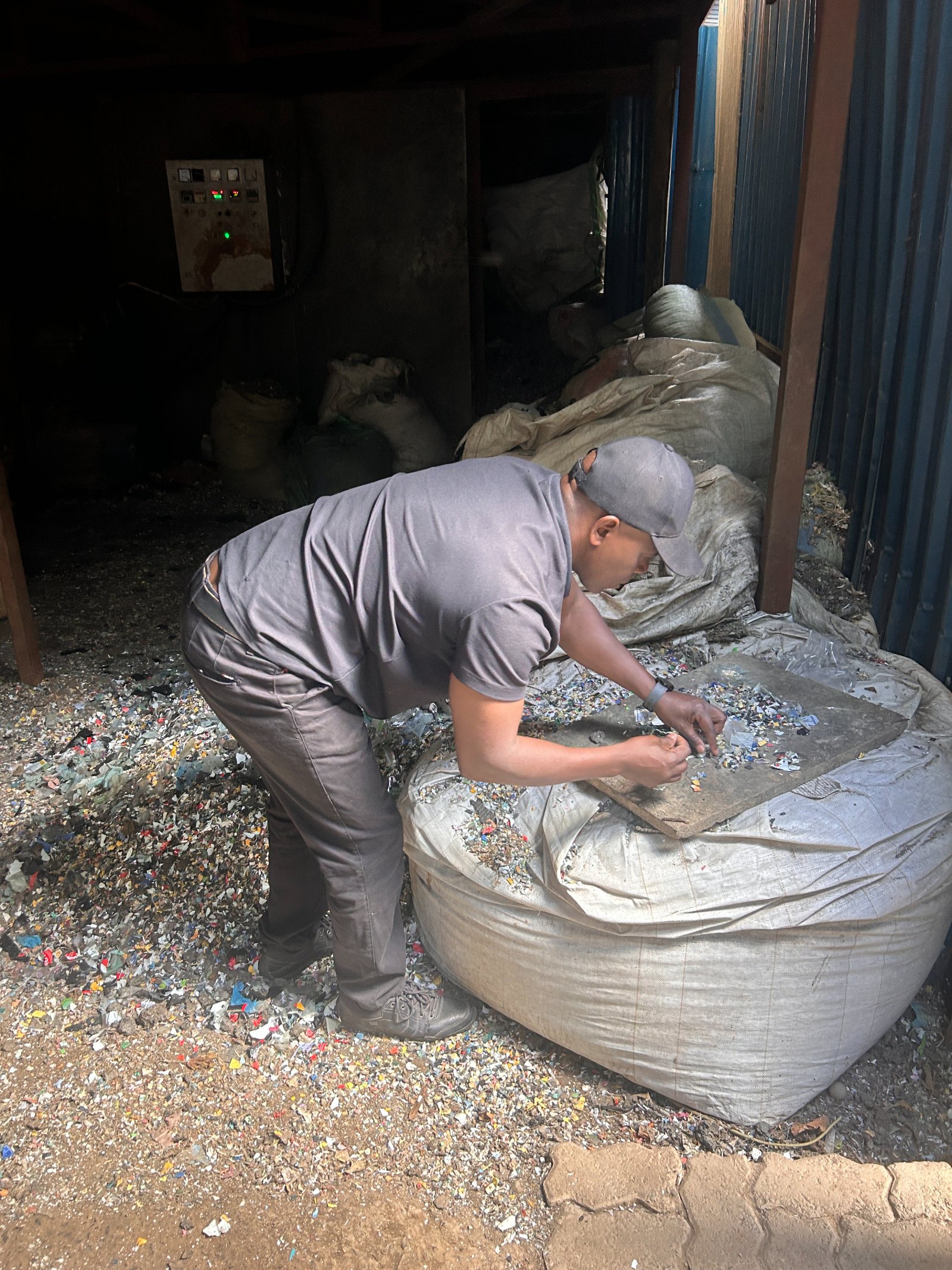 A Silverlink worker examining and sorting shredded plastic feedstock on a board laid over a fibre sack.