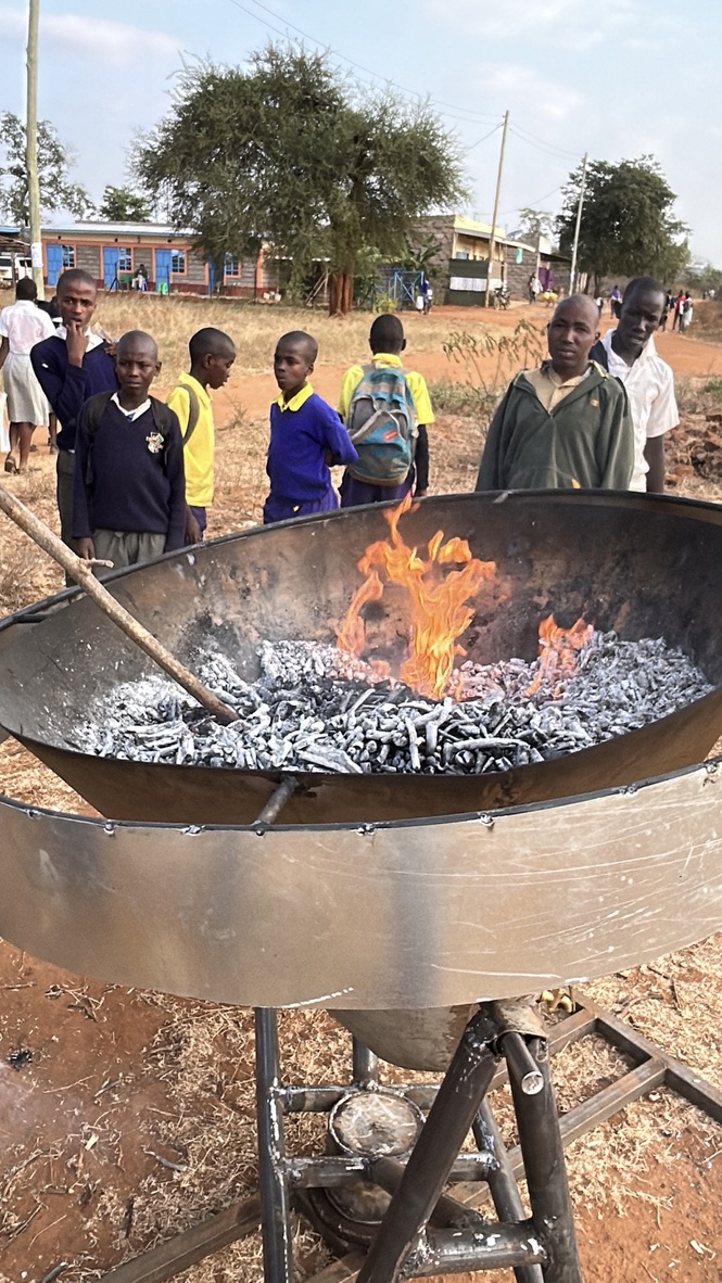 Glowing embers and forming biochar in the Kontiki kiln, with schoolchildren from the local community watching from the roadside.