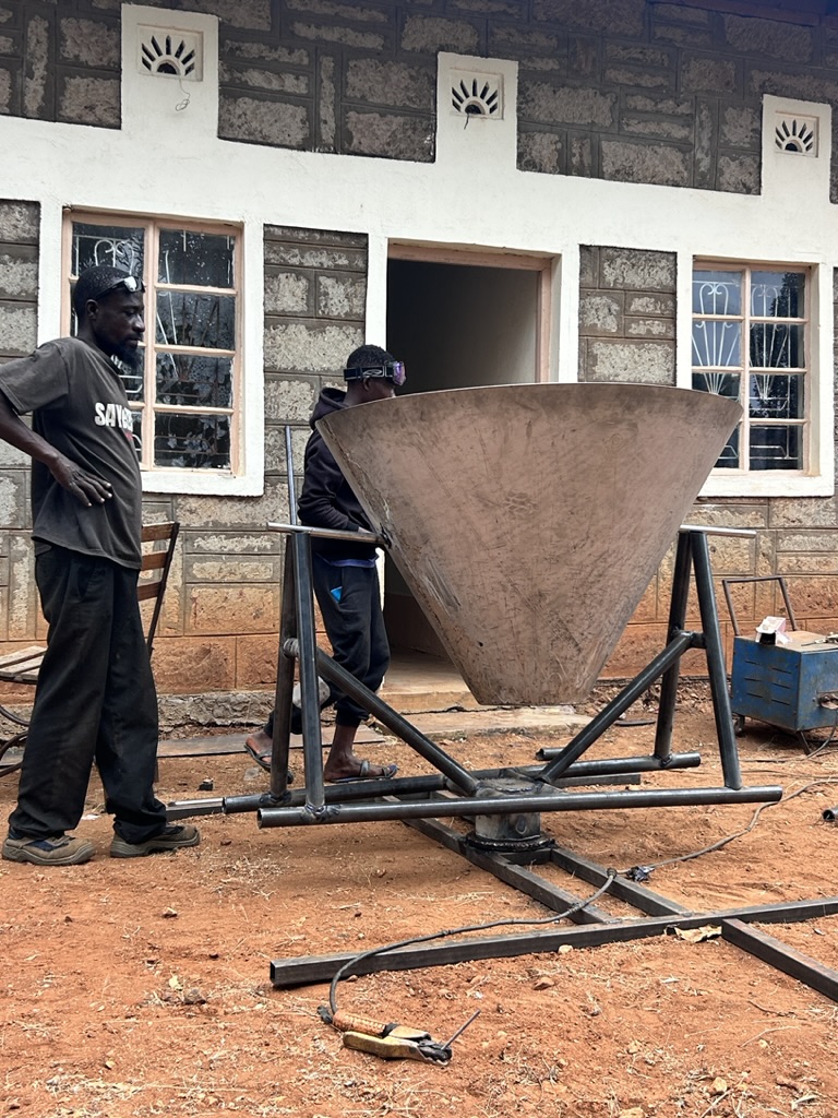 Local metalworkers fabricating the Kontiki kiln cone at the stone building workshop in Wamunyu, with the steel frame visible below.